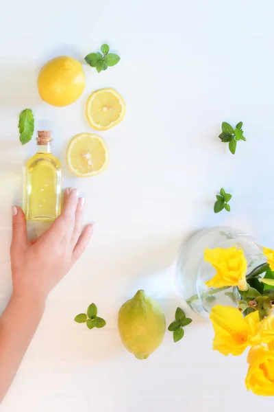女性の手で自然光で撮影したフラットレイフルーツレモン 健康的な新鮮なドリンクレモンを準備 ミントと水 メンタとレモンとヘルシー飲料 レモンオイルとハンド保持ボトル — ストック写真
