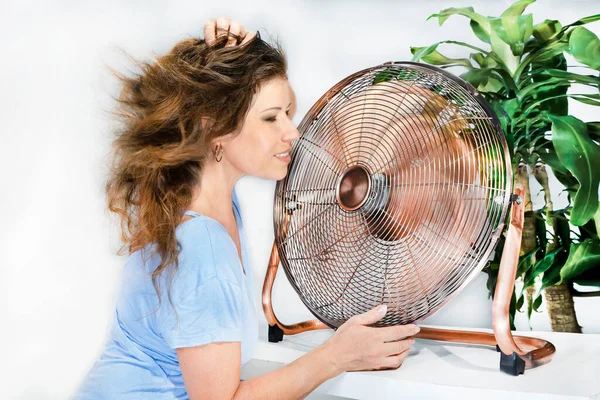 woman holding a fan with her eyes closed, enjoying the wind from the blades.