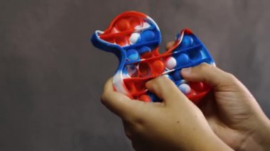 Ördek şeklinde basit bir gamzeli silikon oyuncakla oynayan bir kadının parmaklarının yakın çekimi. Modern çocukların stres önleyici oyuncağı.