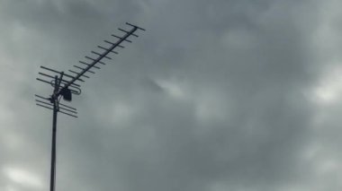 Hızlı uçan gri bulutların arka planına karşı bir televizyon anteni zaman ayarlı. Yakın plan. Kameranın düzgün hareketi