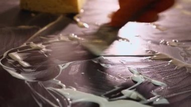 Turuncu eldivenli bir el, tencereyi metal bir kazıyıcı ile temizler. Evde elektrikli soba temizleme fikri. Yakın plan.