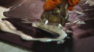 Turuncu eldivenli bir kadının ev yapımı tencereyi metal kazıyıcıyla temizlediği yakın plan bir fotoğraf. Ocakta beyaz bir temizleyici var.