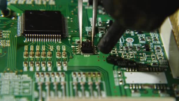 Imagen macroscópica de un reparador utilizando pinzas y una estación de soldadura para instalar un chip en una placa de circuito electrónico. Talleres de electrónica, computadoras, teléfonos y TV. — Vídeos de Stock