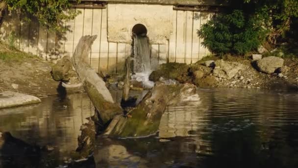 Aguas residuales que fluyen en el río contra el fondo de un enganche que sobresale del agua. Contaminación ambiental. El concepto de ecología. — Vídeos de Stock
