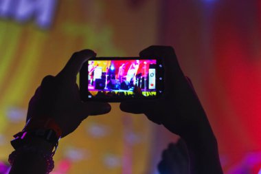 Bir müzik festivalinde sahneyi kaydeden akıllı telefon tutan bir adamın elleri