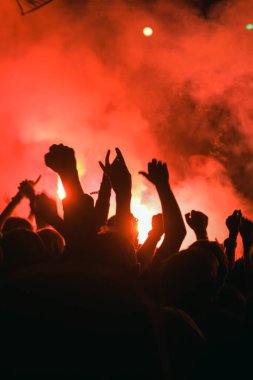 Bir müzik rock festivalinde sahnenin önündeki meşaleden çıkan kırmızı ışığa karşı insanların siluetleri. Konserdeki bir hayran topluluğu.