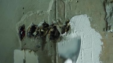 Bir adamın eldivenli eli bir duvara mala yapıştırıyor. Duvardaki delikler eski kablolarla dolu. Yakın plan. Odaları bitirme kavramı