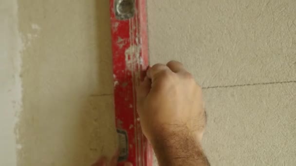 El maestro dibuja una línea con un lápiz en la pared de hormigón. Utiliza un nivel de construcción rojo para la precisión. Primer plano. El concepto de acabado de las habitaciones. — Vídeo de stock