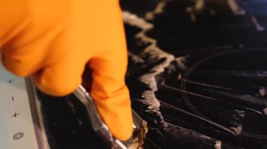 Ev yapımı elektrikli ocağı metal bir kazıyıcıyla temizlemeye yakın çekim. Hob beyaz bir temizleyiciyle kaplanmış.