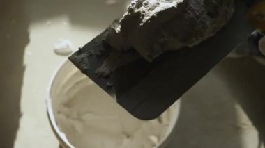 Bir inşaat işçisi alçıyı büyük maladan küçük bir malayla alıp duvara yapıştırıyor. Yakın plan. Odaları bitirme kavramı.