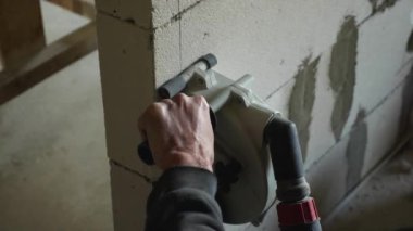 Elektriği yönlendirmek için köpük blokta delik açmak için elektrikli bir aletle erkeklerin ellerine yakın çekim. Odayı tamir etme fikri.