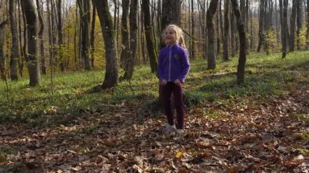 秋の森の中で楽しそうな金髪の子供がボールをしている 背景に落ちた葉や木の幹で 幸せな子供時代の概念 — ストック動画