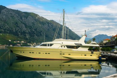 Motor yatı körfeze demirlemiş. Dağın arka planında ve bulutlu mavi gökyüzünde. Suda güzel bir yansıma