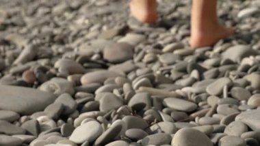 Taş plajda çıplak ayakla yürüyen bir kadın. Yakın çekimler arka plana gidecek. Ve odağını kaybediyor.
