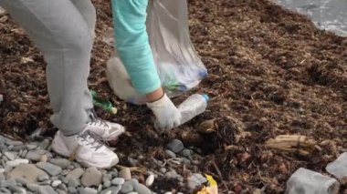 Bir kadın poşette plastik çöp topluyor. Bir gönüllü plastik şişelerin sahil şeridini temizliyor. Ekoloji kavramı
