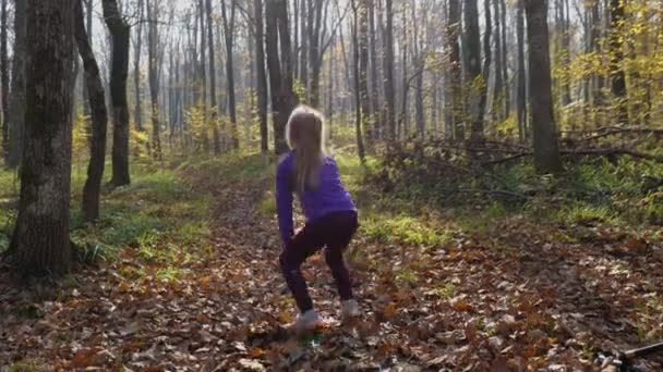 ブロンドの女の子の子供が秋の森の中でボールを投げ キャッチします 背景に落ちた葉や木の幹で 幸せな子供時代の概念 — ストック動画
