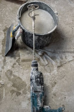 Yanında iki mala olan plastik bir kova su ve kuru karışımları karıştırmak için eklenmiş kirli bir delik delgisi. Üst taraf manzarası. Yerler kuru alçıyla kaplanmış. Onarım ve dekorasyon