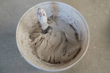 Beyaz plastik bir kovada, taze sıva karışımı. Karışımın içine bir mala sıkışmış. Yukarıdan bak. Oda yenileme konsepti