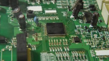 Bir tamircinin cımbız ve lehim kullanarak işlemciyi tahtaya monte ettiği makro bir video. Mikroçipin altında kızarıklık var. Elektronik, bilgisayar ve TV tamirhanesi.