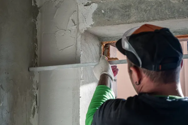 A plastered wall is being leveled with an aluminum rule. The concept of room finishing