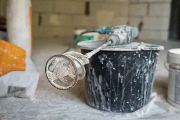 On the black bucket lies a hole punch with a dry mixer nozzle. In the background there are paper bags of plaster. Professional power tool for repairs. Selective focus