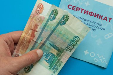 Covid-19 aşı sertifikası için bir el para tutuyor. Mavi arka plan. Yakın plan. Çeviri: yeni bir koronavirüs enfeksiyonuna karşı aşı sertifikası COVID-19