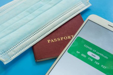 Geçerli bir covid-19 dijital aşı sertifikalı akıllı telefon ekranının yakın çekimi. Pasaport ve sağlık maskesinin yanında.