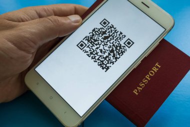 Bir adamın elinde pasaport ve ekranda QR-19 dijital aşı sertifikası olan bir akıllı telefon var. Yakın plan. Mavi arkaplan
