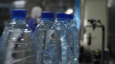 Kameraya doğru giden mavi plastik bir su şişesinin yakın plan görüntüsü. Gıda işleme tesisinde maden suyu üretimi
