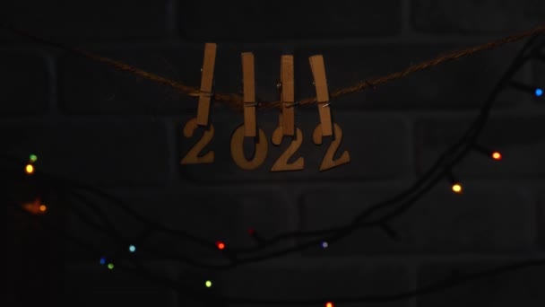 2022年的木制编号用衣针挂在背景上的一根绳子上 带有五彩缤纷的花环灯 一束光线直射向这些数字 新年快乐 — 图库视频影像