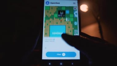 Kullanıcı, cep telefonu ekranındaki NFT koleksiyonunu parmaklarıyla kaydırıyor. OpenSea platformunda dijital sanat eserlerine göz atın. Yakın plan. Rusya, Krasnodar Bölgesi, 25 Kasım 2021