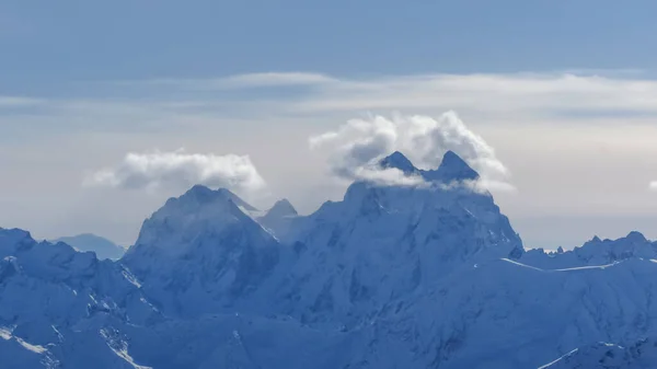 白雪覆盖的陡峭的山峰 山顶上笼罩着一片云彩 背景是一片蓝天 美丽的冬山风景 — 图库照片