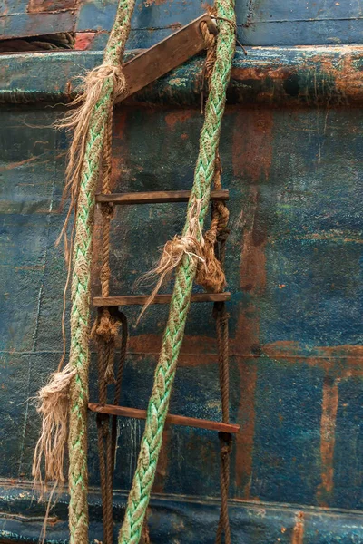 A homemade ladder made of ship\'s ropes, metal rope, and planks hangs from an abandoned ship