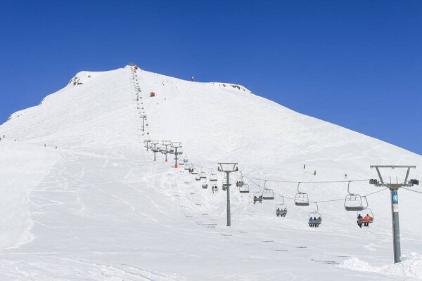 The chairlift to the top of the mountain. To the left of it and under it is a ski slope. In the background is a clear blue sky