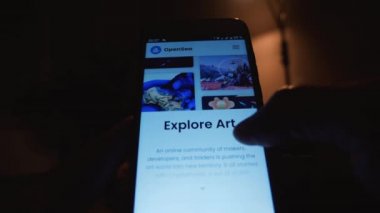 Karanlık bir odada akıllı telefon koleksiyonunda parmaklarıyla gezen bir adam. OpenSea web sitesinde dijital sanata bakmak. Yakın plan. Rusya, Krasnodar Bölgesi, 25 Kasım 2021
