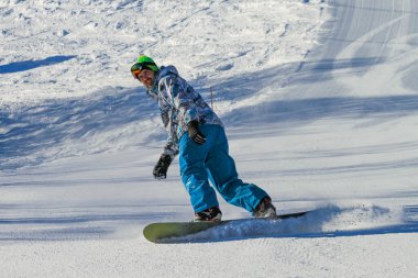 Yakışıklı genç bir adam kayak tahtasında kayak pistinden aşağı kayıyor. Kar tahtasının altından uçup gidiyor. Yokuşta yalnız bir snowboardcu. Tatillerde kış sporları