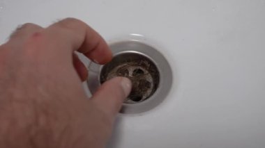 Sıhhi tesisatı gevşek kadın saçlarıyla tıkamak. Bir adamın eli banyo giderinden bir tutam saç çekiyor. Saç dökülmesi sorunu..