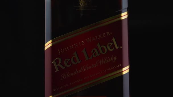 Närbild av en flaska Johnnie Walker Red Label Scotch Whisky mot en mörk bakgrund. Kameran flyger runt. Parallellaxeffekt. — Stockvideo