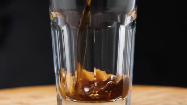 Egy közeli kép egy sötét szénsavas italról, amit egy pohárba öntenek. A kamera repked. Párhuzamos hatás. — Stock videók