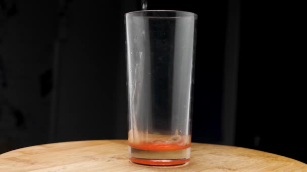 Mutfak tahtasının üzerinde duran bardağa yakın çekim yapan su dökülür. Kamera etrafta uçuyor. Parallaks etkisi. Koyu arkaplan. — Stok video