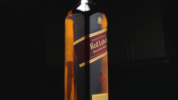 Sebotol Johnnie Walker Red Label wiski dengan latar belakang gelap. Kamera terbang di sekitar. Efek Parallax. Warna Amber dari minuman.