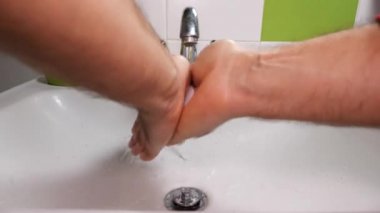 Banyodaki adam soğuk musluk suyunun altında ellerini sabun ve suyla dikkatlice yıkar. Sonra onları mavi bir havluyla siler. Hijyen kavramı ve koronavirüs salgınının önlenmesi