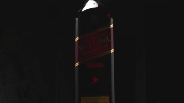 Botella Johnnie Walker Red Label sobre fondo oscuro. La cámara vuela alrededor. Efecto paralelo. Whisky escocés mundialmente famoso. — Vídeo de stock