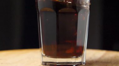 Buz küplerinin karbonatlı bir bardağa düşüşünün hızlandırılmış görüntüleri. Kamera etrafta uçuyor. Parallaks etkisi