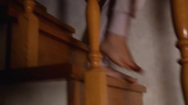 Ağır çekimde kamera, tahta bir merdivenden inen gri pantolonlu bir kadının çıplak ayaklarını takip ediyor. Balyaların arasından yan görüş. Evde loş bir ışık var.