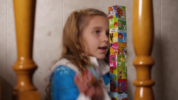 Egy Gyönyörű Szőke Kislány Kék Köntösben Kockákból Álló Tornyot Épít — Stock videók