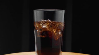 Mutfak tahtasının üzerinde buzlu bir bardak ve karbonatlı bir içecek duruyor. Kamera etrafta uçuyor. Parallaks etkisi. Karanlık arka plan. Yakın plan.