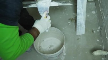 Bitiş uzmanı kalan alçıyı bir kovada toplar ve bir malaya yapıştırır. Yakın plan. Odaları bitirme konsepti. Rusya, Krasnodar, 20 Ekim 2021