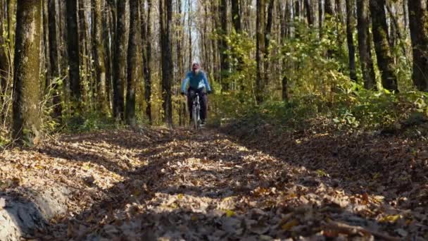 Велосипедист Смотрит Камеру Едет Лесной Дороге Усеянной Опавшими Листьями Низкий — стоковое видео