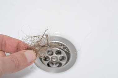 A man's fingers take a bundle of hair out of a sink drain. Close-up. The problem of hair loss after chemotherapy